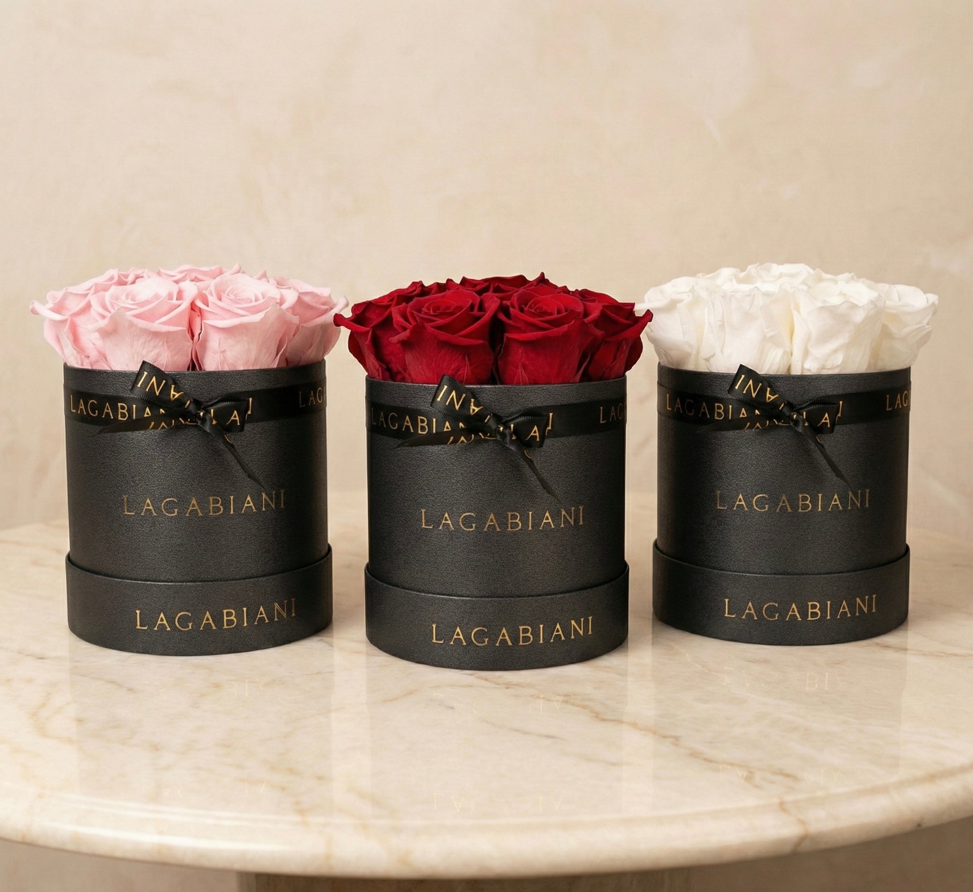 Three black Lagabiani boxes with pink, red, and white roses on a marble surface.