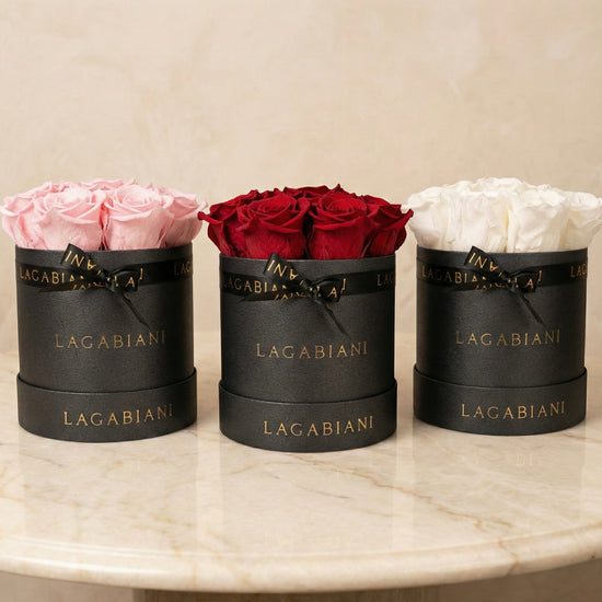 Three black Lagabiani boxes with pink, red, and white roses on a marble surface.